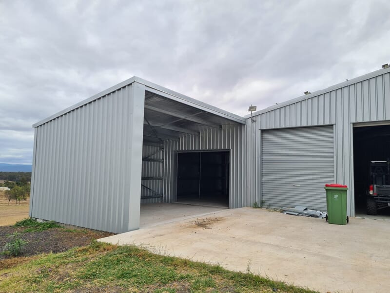 Open-bay shed with roller door beside a larger machinery shed